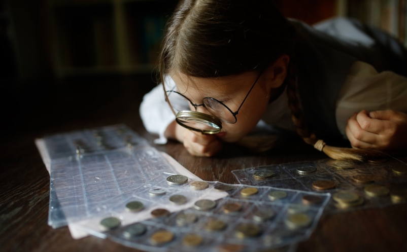 Kid in glasses with magnifying glass and collection of coins, numismatics, money